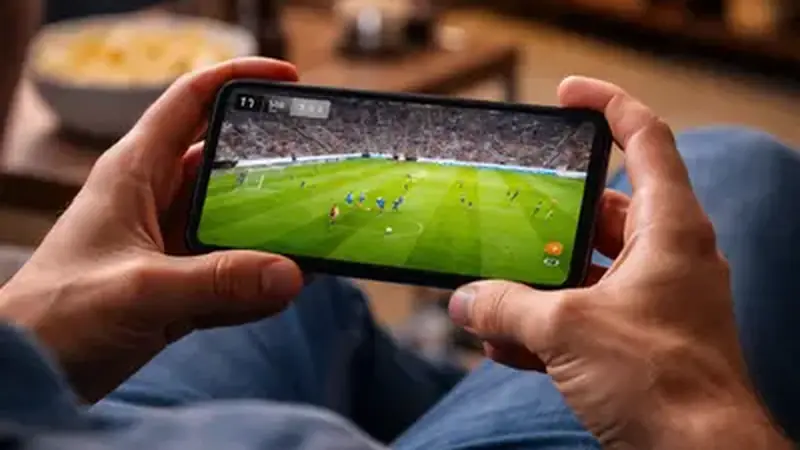 Hand holding a smartphone showing a live football match at a stadium